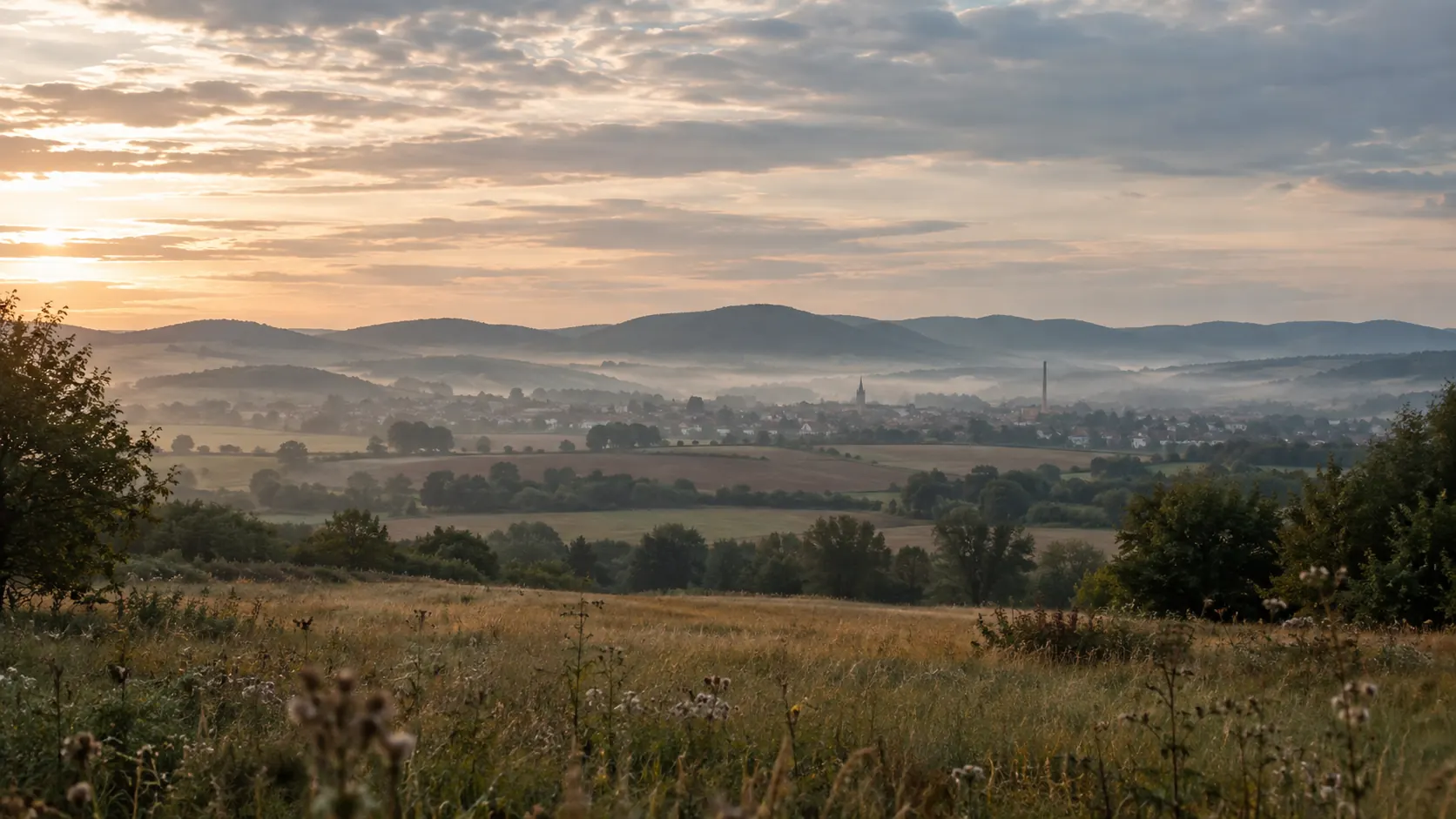 Pohľad z lúky na mesto v hmlistom údolí pri východe slnka
